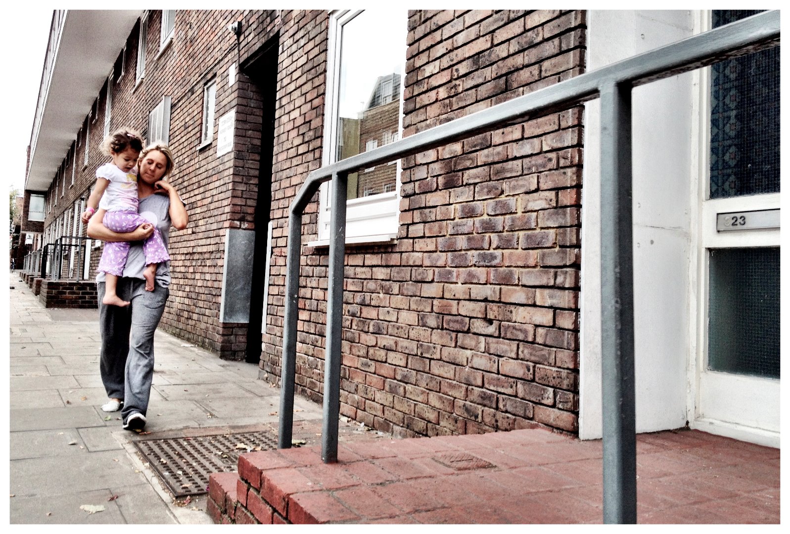 Woman carrying a young girl outside a council estate